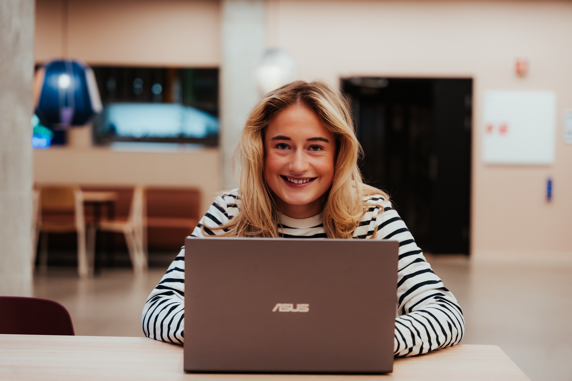 Kvinnelig student sitter bak bærbar PC og smiler til kamera