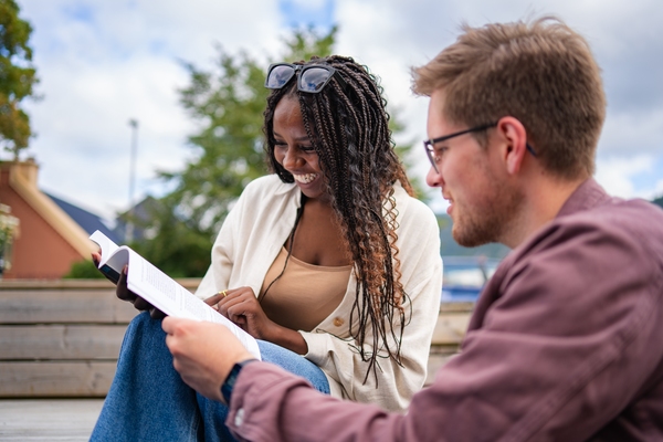 Foto av to studenter som sitter og leser fra en bok. Foto
