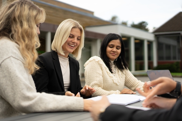 Tre student som sitter og leser fra en notatbok. Foto