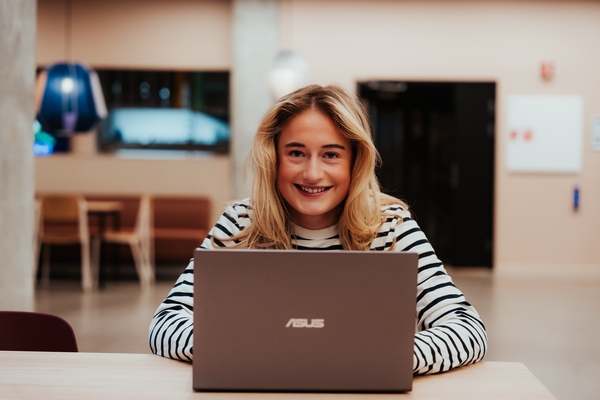Kvinnelig student sitter bak bærbar PC og smiler til kamera