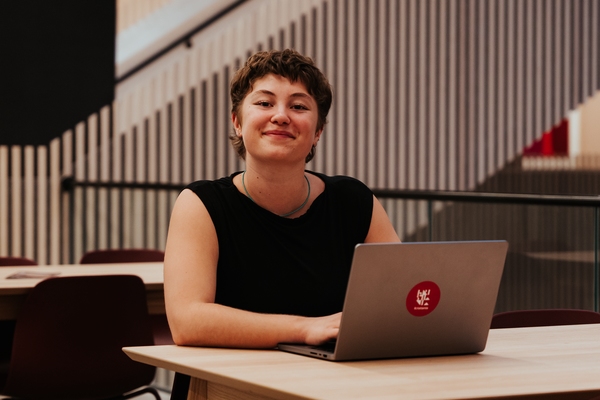 Kvinnelig student sitter ved bærbar PC og smiler til kamera