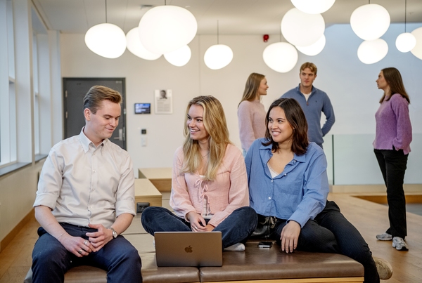 Tre studenter på NHH ser på hverandre og smiler. Foto
